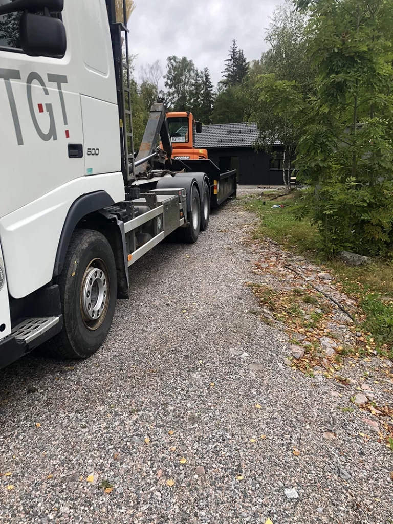 Grävfirma lastar på grävmaskin på lastbil.